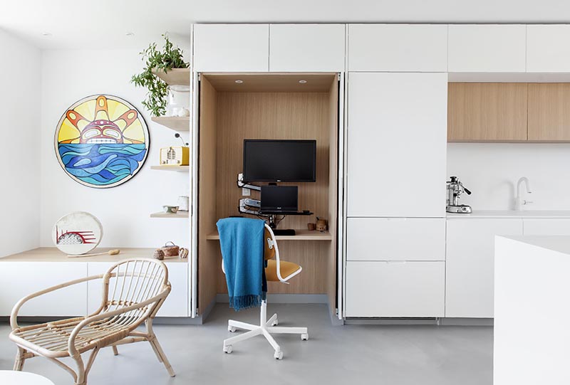 A small wood lined home office located within minimalist white  kitchen cabinets.