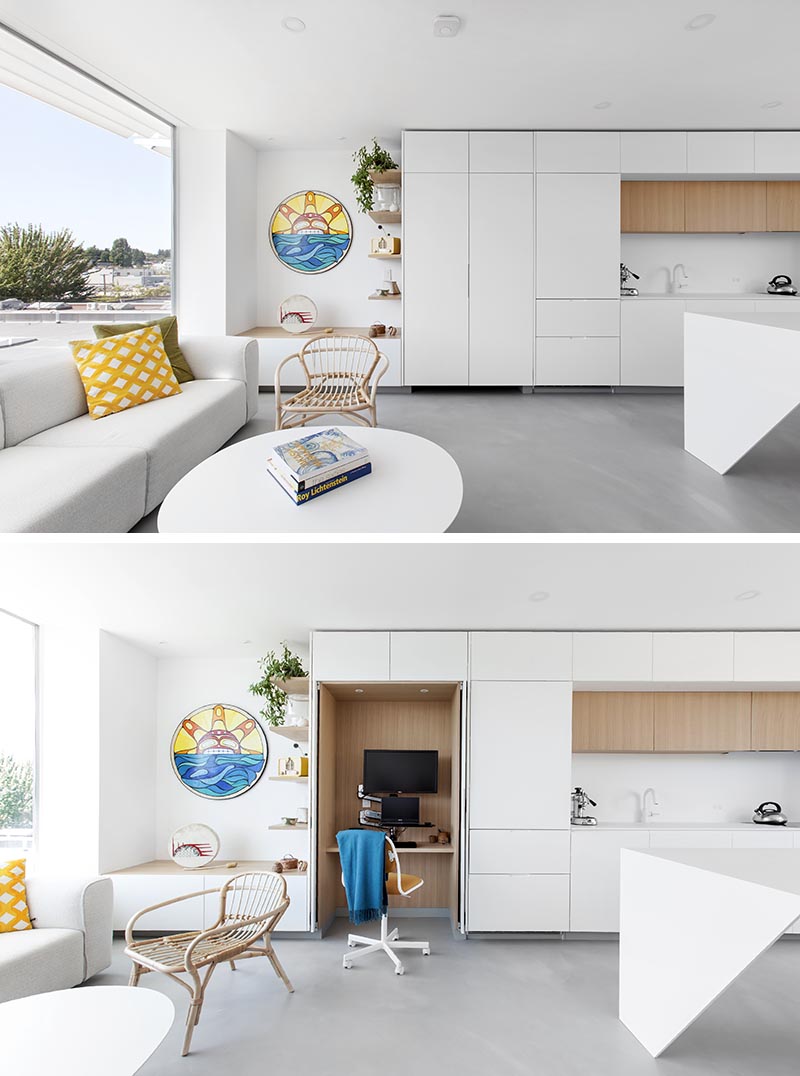 Minimalist white kitchen cabinets open to reveal a small wood lined home office.