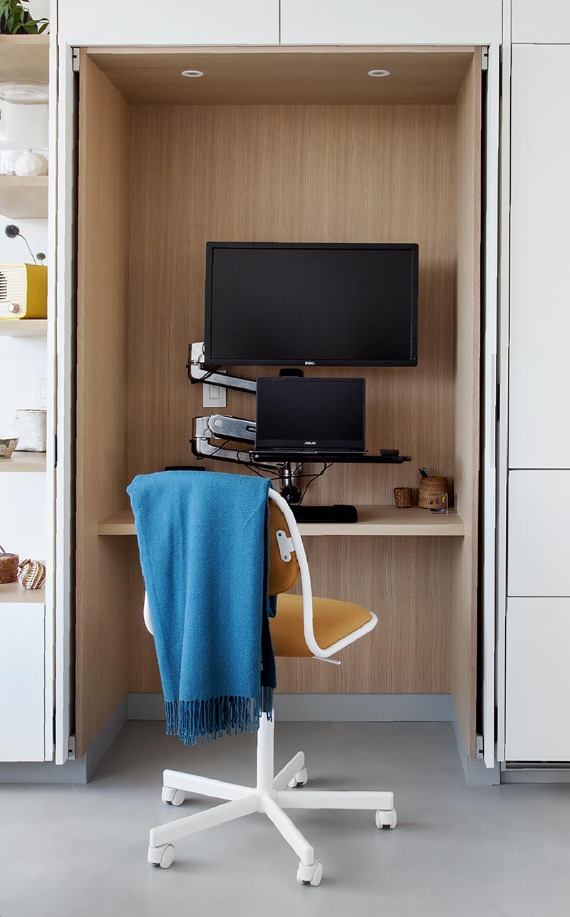 A small home office is tucked away within minimalist white kitchen cabinets.