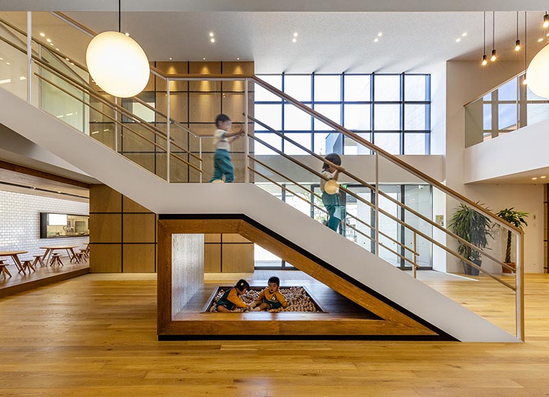 Located underneath the lower half of these kindergarten stairs is a wood framed area that's home to kids play area with a small ball pit. #KidsPlayArea #UnderStairDesign #KidsBallPit #InteriorDesign