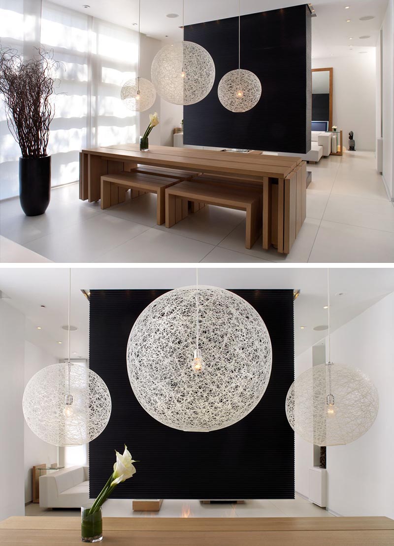 A black room divider (or partition wall) creates a striking backdrop for the three white pendant lights above a wood dining table.