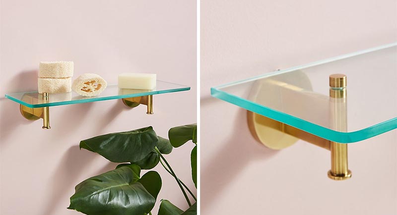 Modern bathroom shelf that has a thick glass top and brass supports.