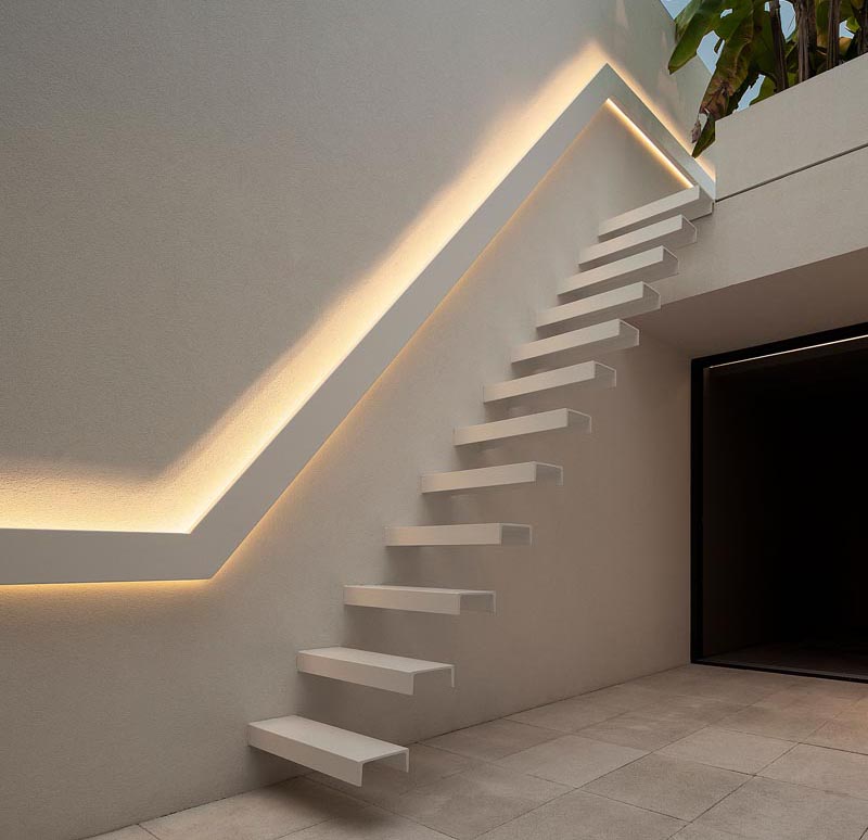 A backlit handrail runs alongside cantilevered stairs.