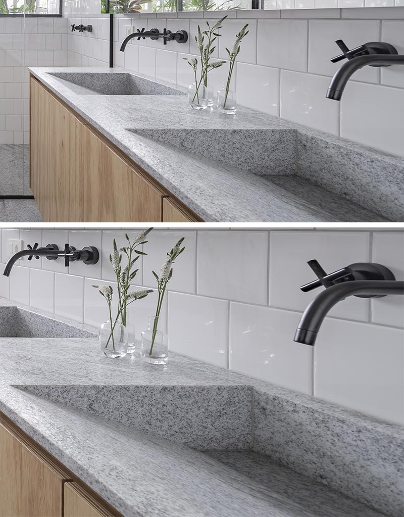 The natural wood vanity in this modern bathroom is topped with a Brazilian grey and white granite named "Branco Sao Paulo" in a matte finish, however it's the dual sinks with a sloped interior that are the focal point. #ModernBathroom #GraniteBathroomCountertop #GreyBathroom #ModernVanity