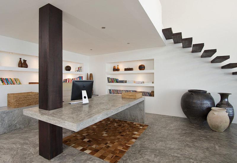 A concrete desk uses a wood column as support in this home office that also features built-in shelving.