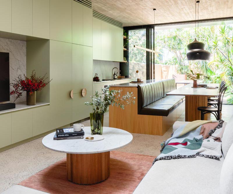 A modern light green kitchen with an island that transitions into a bench for dining table seating.
