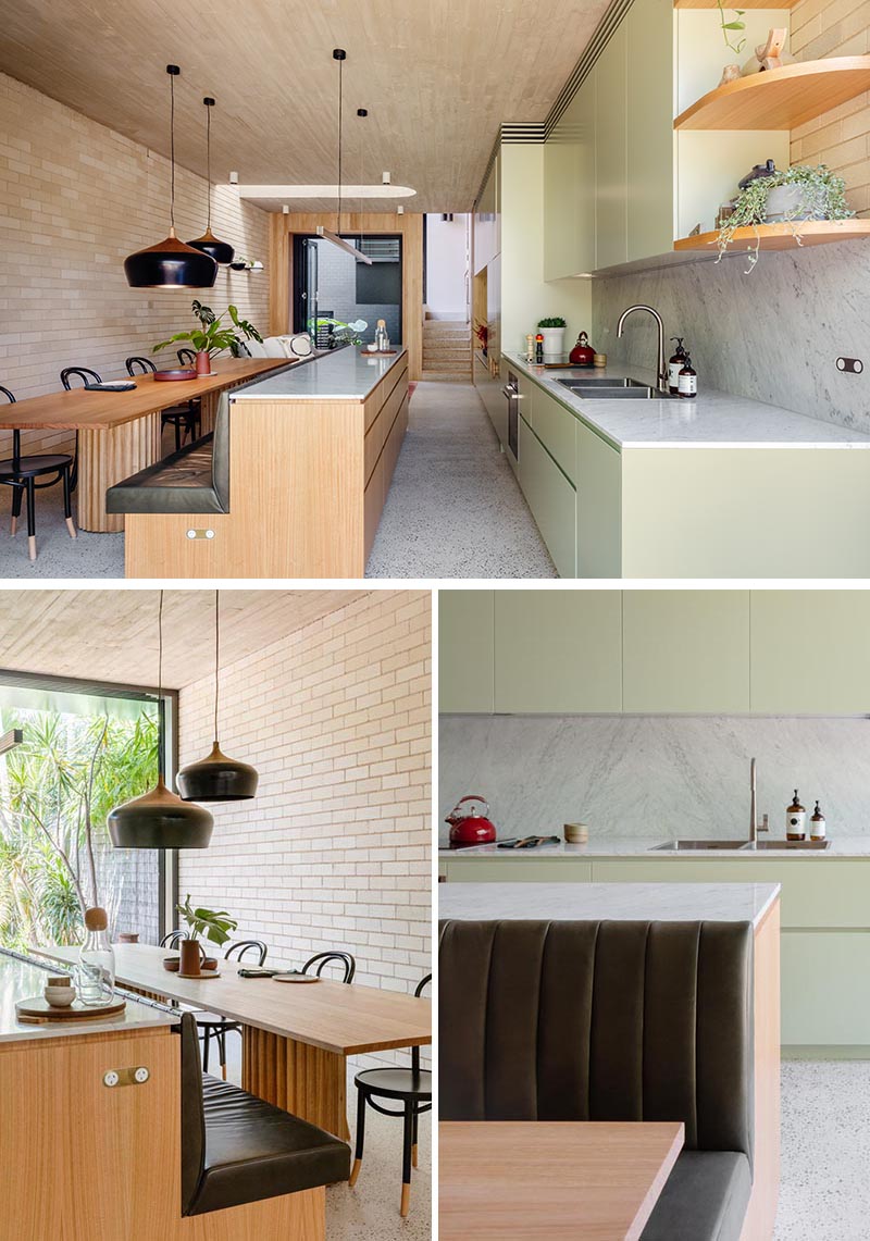 A light green kitchen has a wood island that transitions into a banquette bench for the dining table.