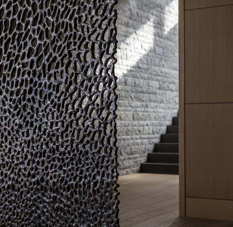 An artistic bronze partition screen separates the dining room from the entryway of a modern house.