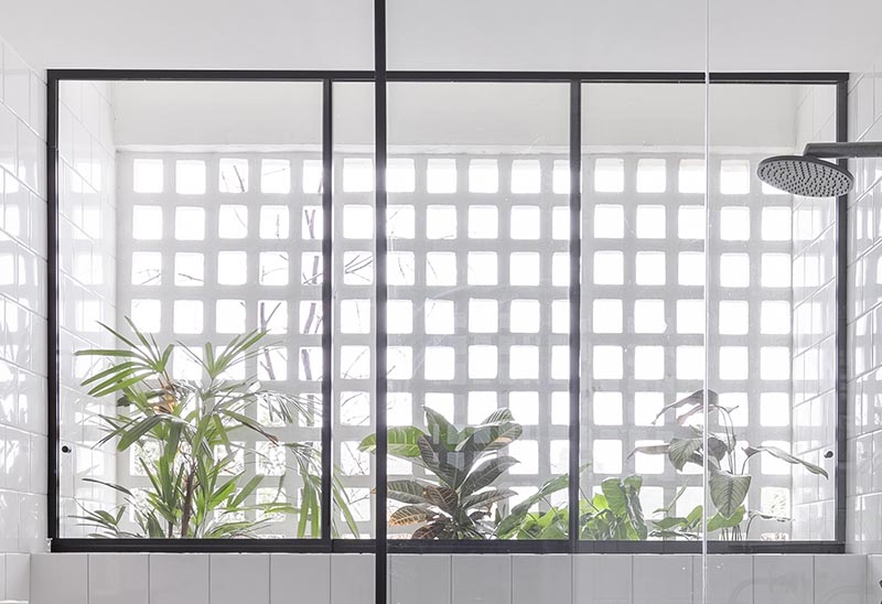 In the shower of this modern bathroom, there's a black-framed three pane window that looks out to a collection of plants that are located between the bathroom wall and the facade of the apartment. #BlackFramedWindow #BathroomDesign #PlantIdeas