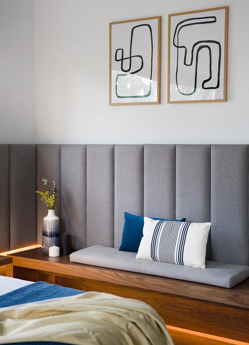 A modern wood bench with a grey cushion and minimalist line artwork on the wall above.