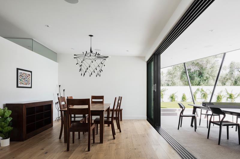 A modern dining room with stacked sliding glass doors, white walls, and dark wood furniture.