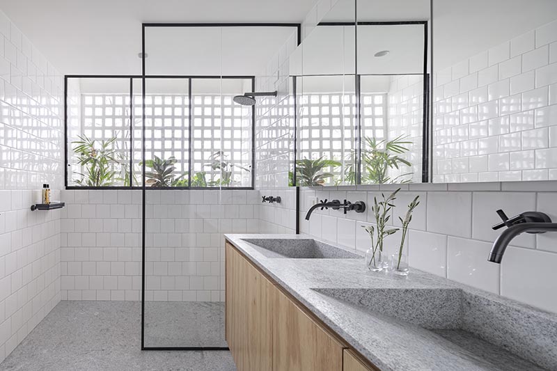 BLOCO Arquitetos has created a bright and modern bathroom featuring wood, grey granite, square white tiles, and black accents. #ModernBathroom #BathroomDesign #BrightBathroom #GreyAndWhiteBathroom