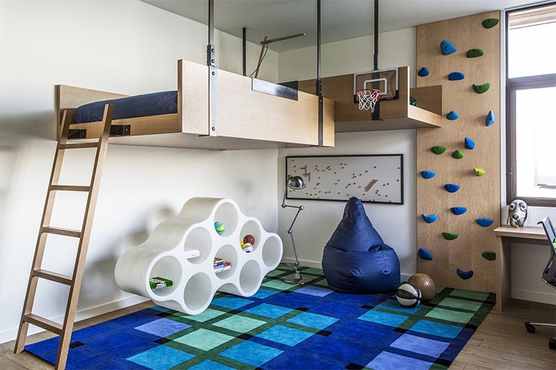 A kids bedroom with a loft bed, a mini basketball hoop, a rock climbing wall, study desk, and play area.