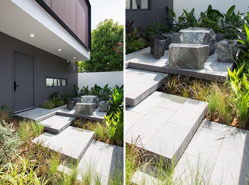 A front garden with overlapping steps, tropical plants, and a small seating area.