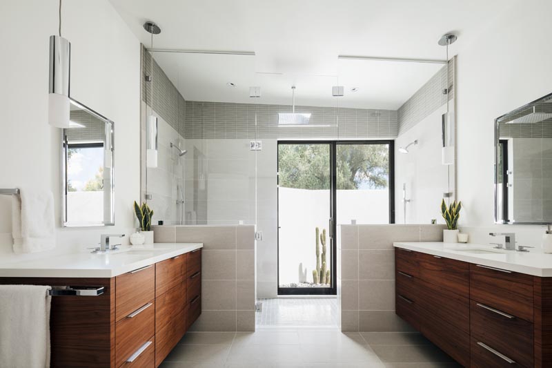 A modern master bathroom with separate dark wood vanities, and a large shower for two.