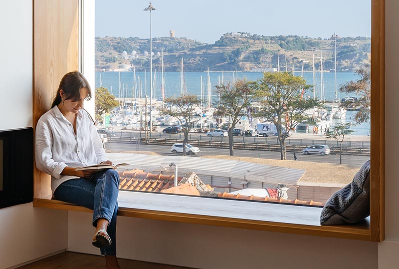 Aurora Arquitectos has designed a house for a family in Lisbon, Portugal, and to make the most of the street and water views, the architects included a large window seat. #WindowSeatIdeas #WindowSeat #WoodLinedWindowSeat #PictureWindow