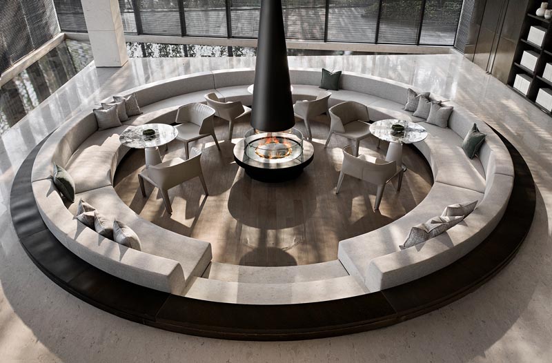 This modern sunken conversation pit, which was designed as a warm and pleasant space for potential customers to talk, offers custom seating that wraps around the interior of the circular shape, with enough room for small tables to also be included. #ConversationPit #SunkenSeating #InteriorDesign #Fireplace