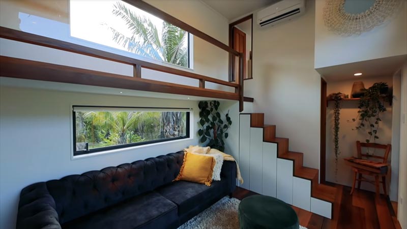 This tiny house has stairs that connect to a walkway that leads to the two bedrooms.