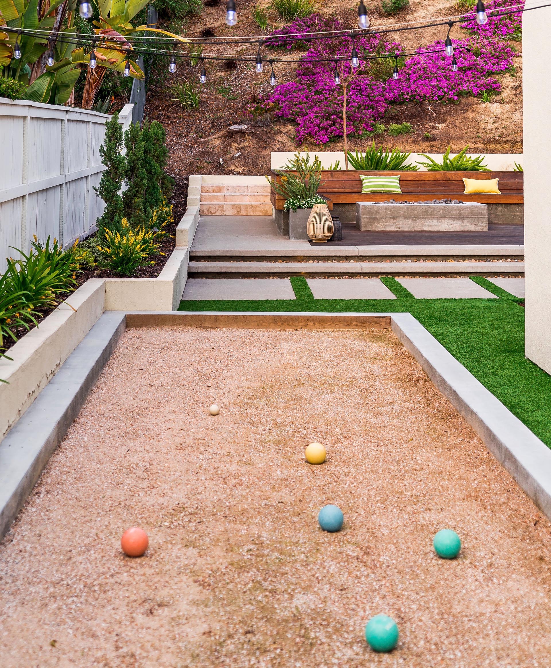 A modern yard with a raised seating area and fire pit, and a bocce court.