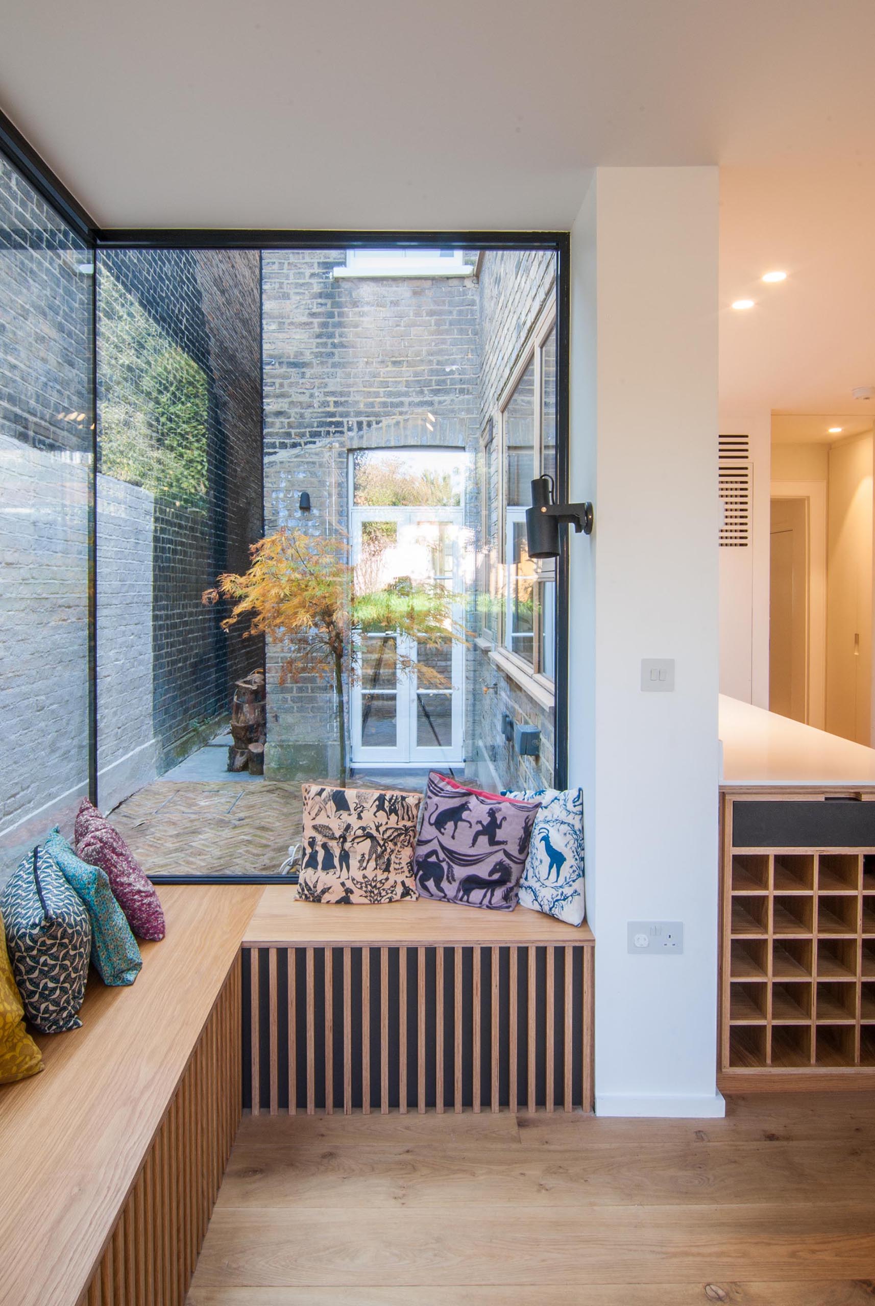 A corner window seat with cushions looks out to a side garden