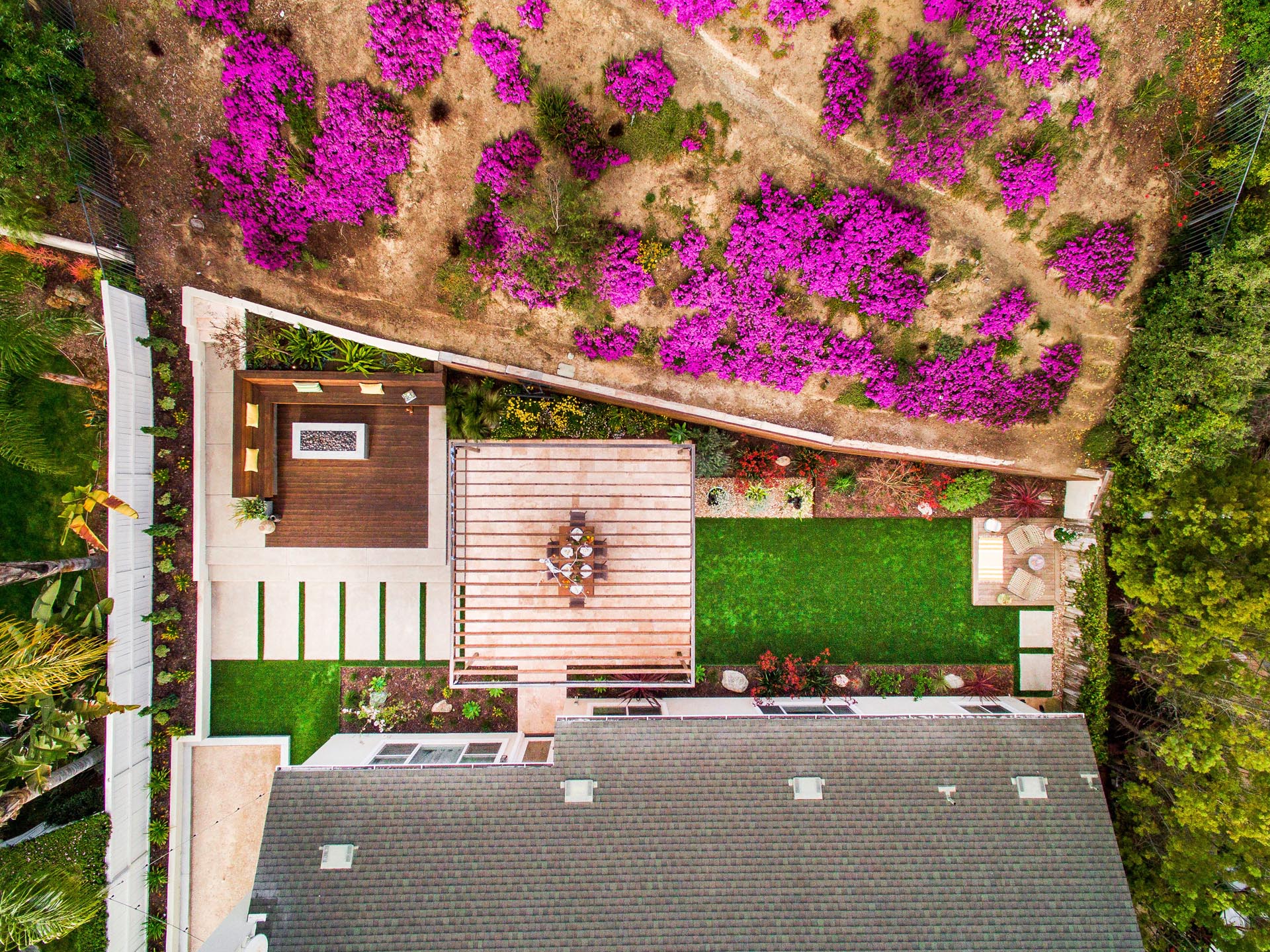 A modern yard with seating area, fire pit, built-in benches, steel planters, alfresco dining under a pergola, a bocce court, and artificial grass.