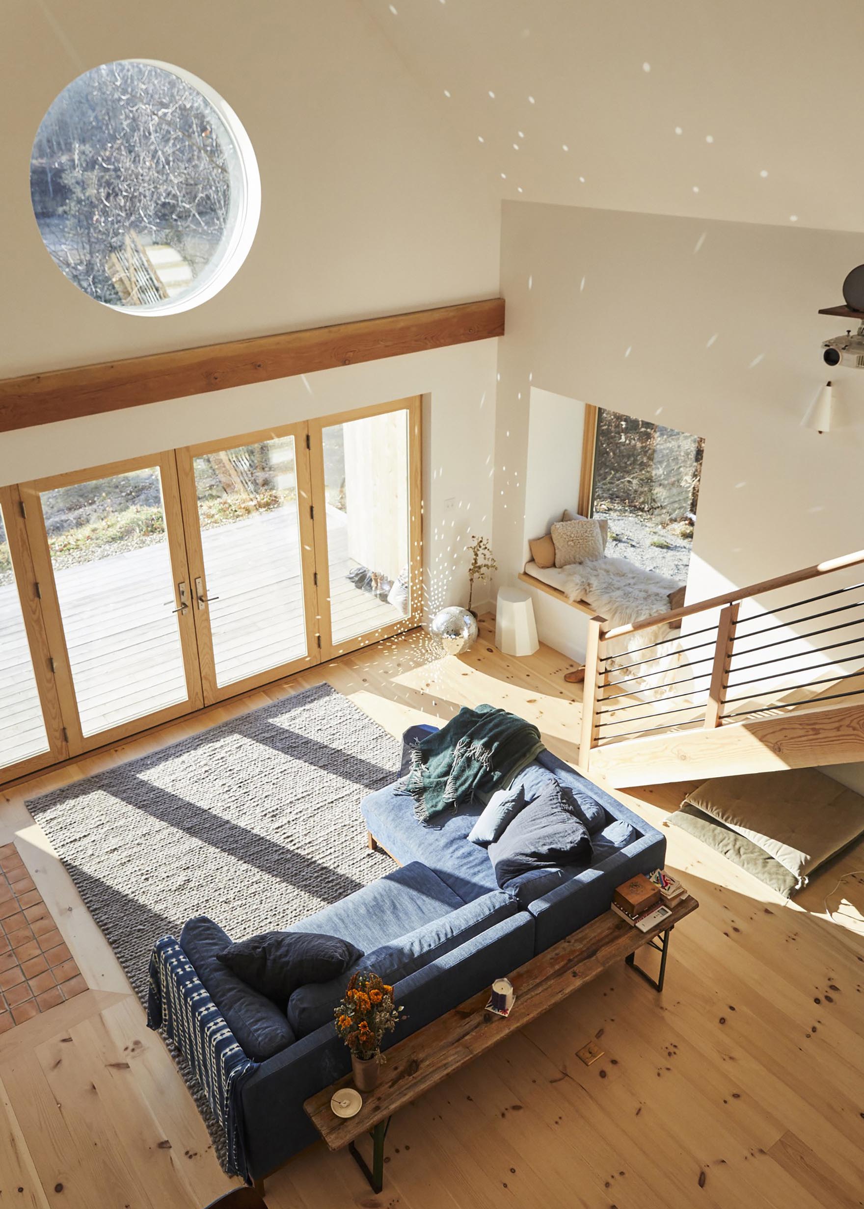 A Scandinavian inspired living room with blue couch, a large grey rug, a cozy window seat, and a mirror ball that scatters the sunlight.