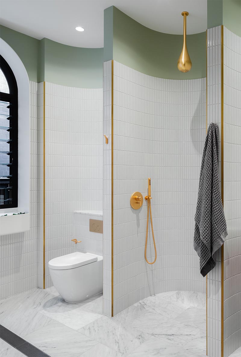 A modern bathroom with tiled curved walls creates different sections for the vanity, shower, and toilet.