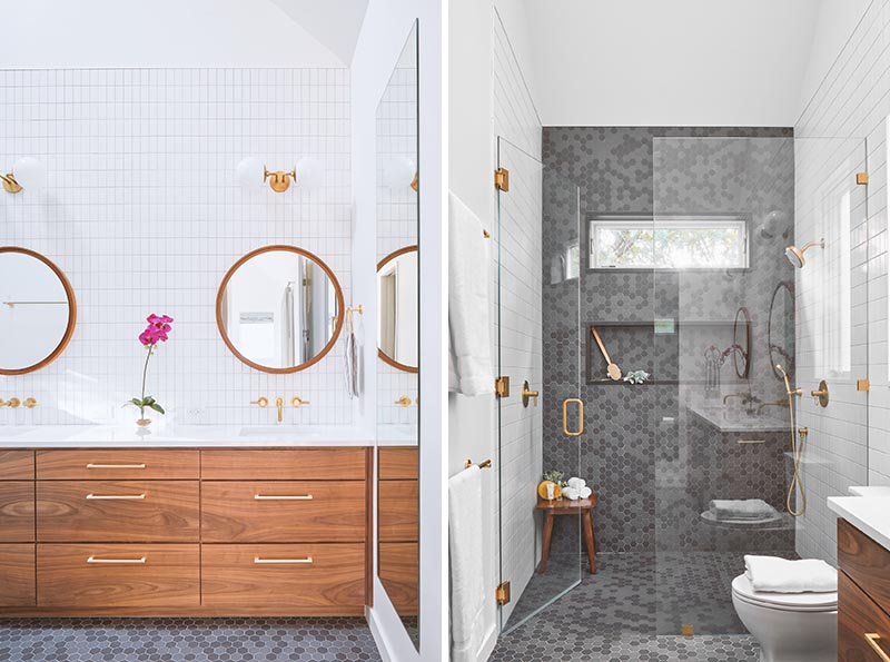 A modern bathroom with a wood vanity, gold accents, round mirrors, and grey hexagonal tiles in the shower and on the floor