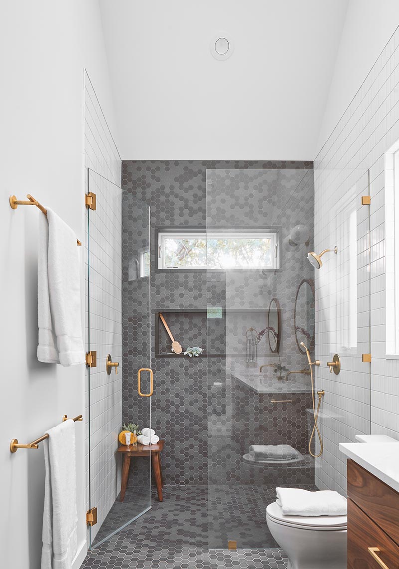 A modern shower with grey hexagonal tiles, a shower niche, and a frameless glass shower door.
