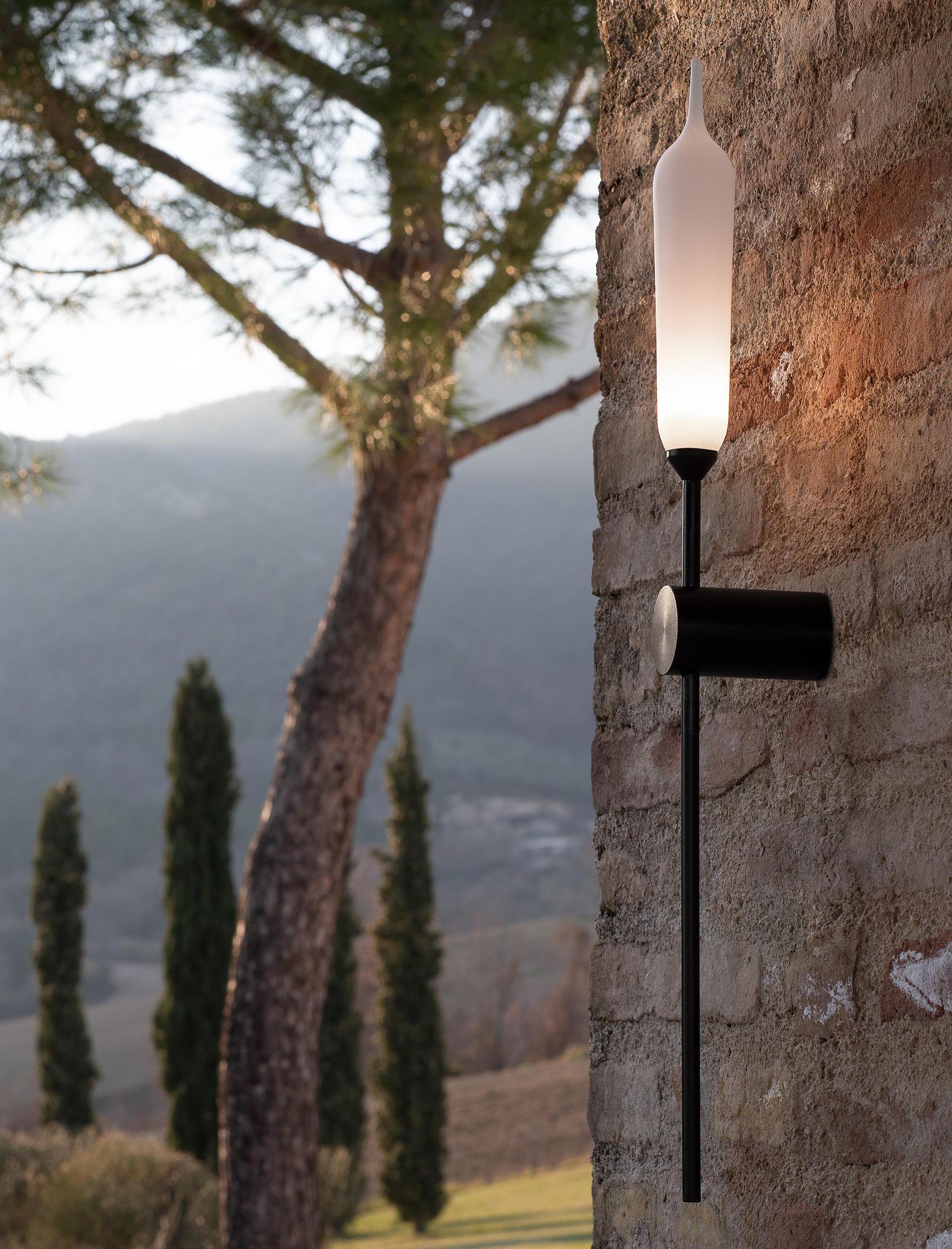 A modern outdoor wall lamp with a matte white resin diffuser and a black support.