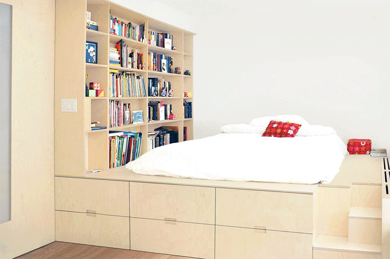 A small apartment features a custom designed platform bed that's been raised up to create hidden storage.