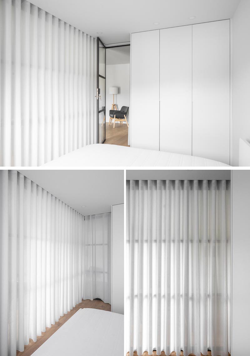Floor to ceiling white curtains create privacy for a glass enclosed bedroom.