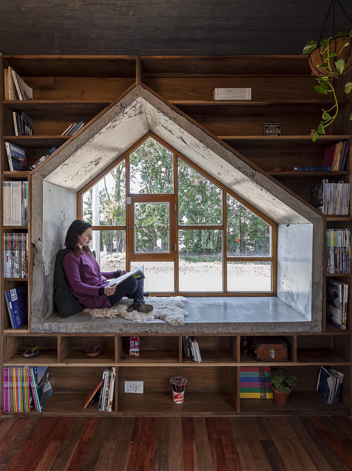 A window seat surrounded by dark wood shelving, has an interior of raw concrete.