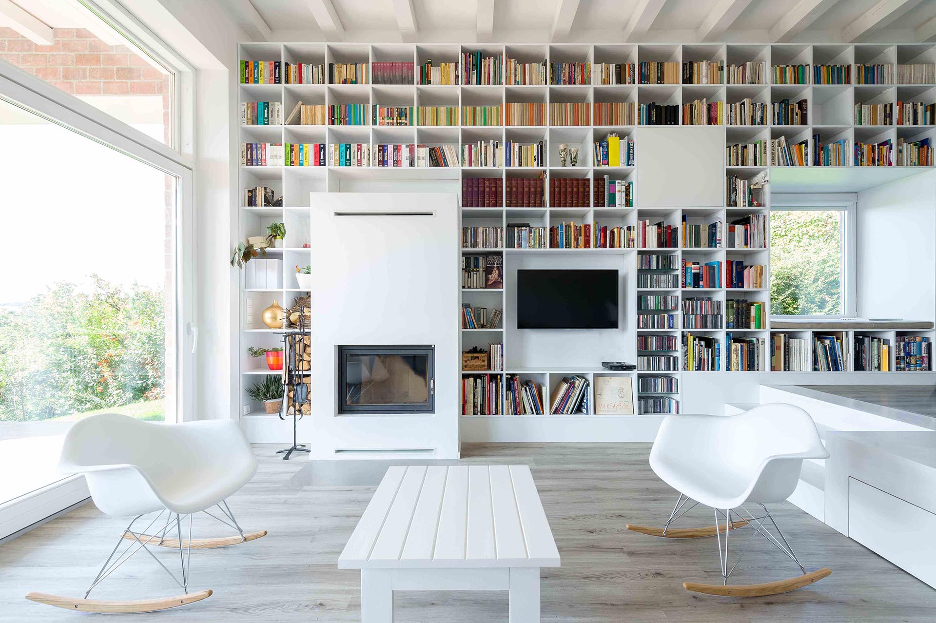 A full wall of white shelving that surrounds a fireplace, television, and windows.