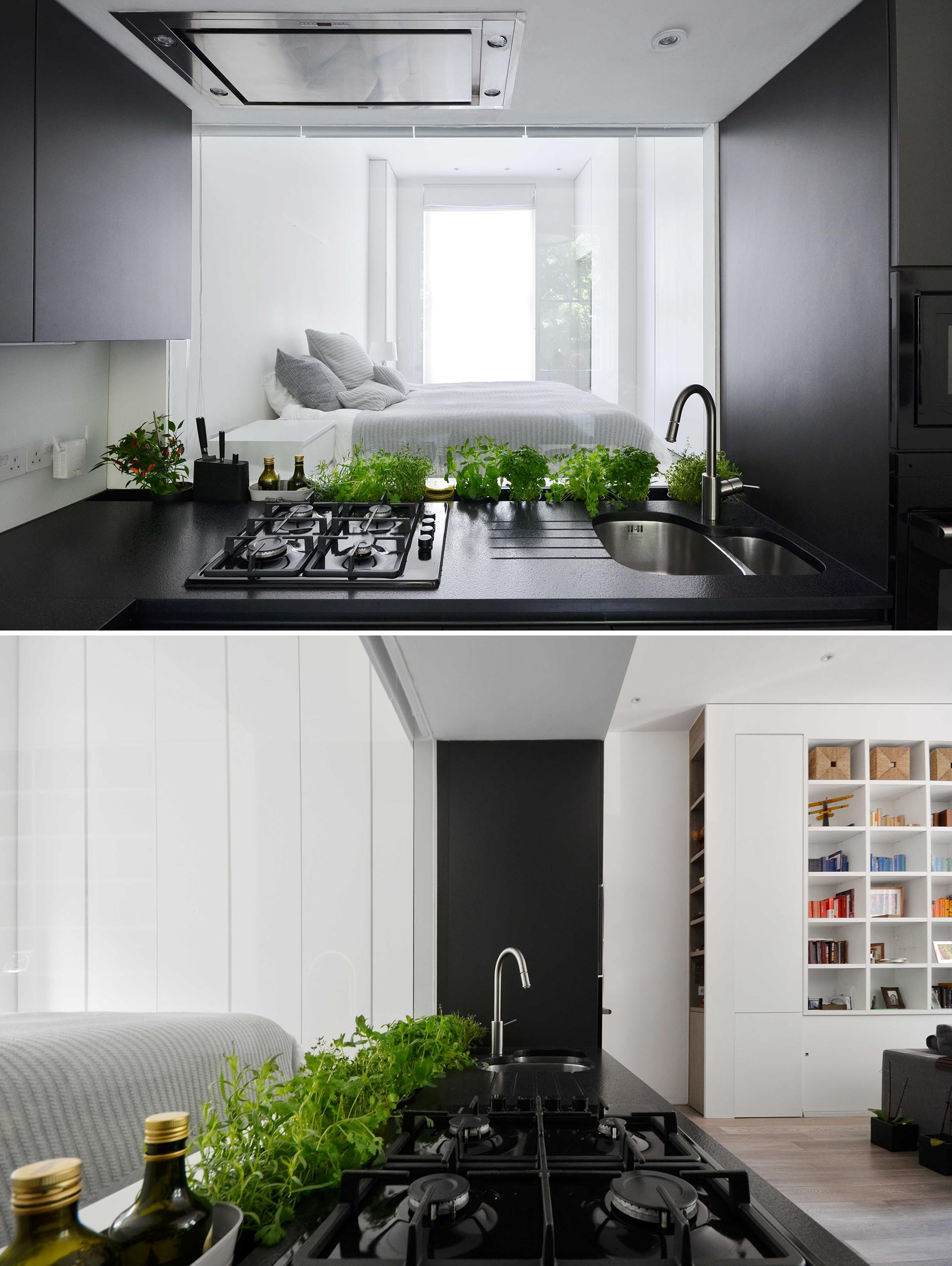 A matte black kitchen with a glass backsplash that acts as a window with views of the bedroom.