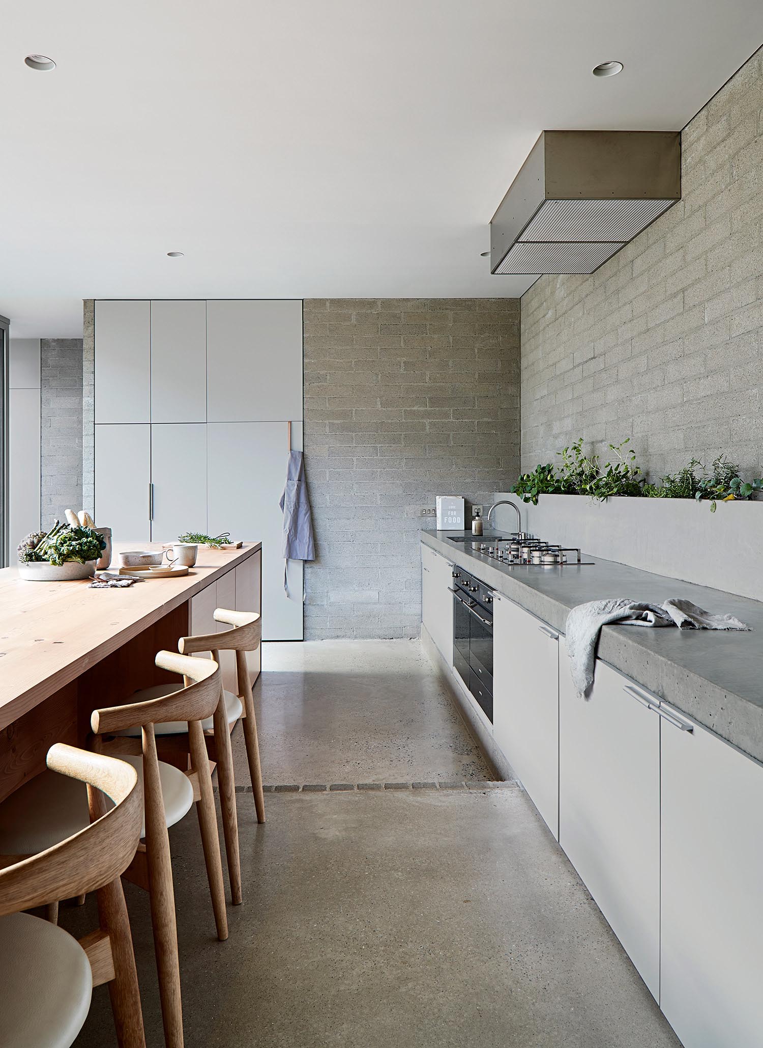 A modern grey kitchen with a wood island and concrete floors.