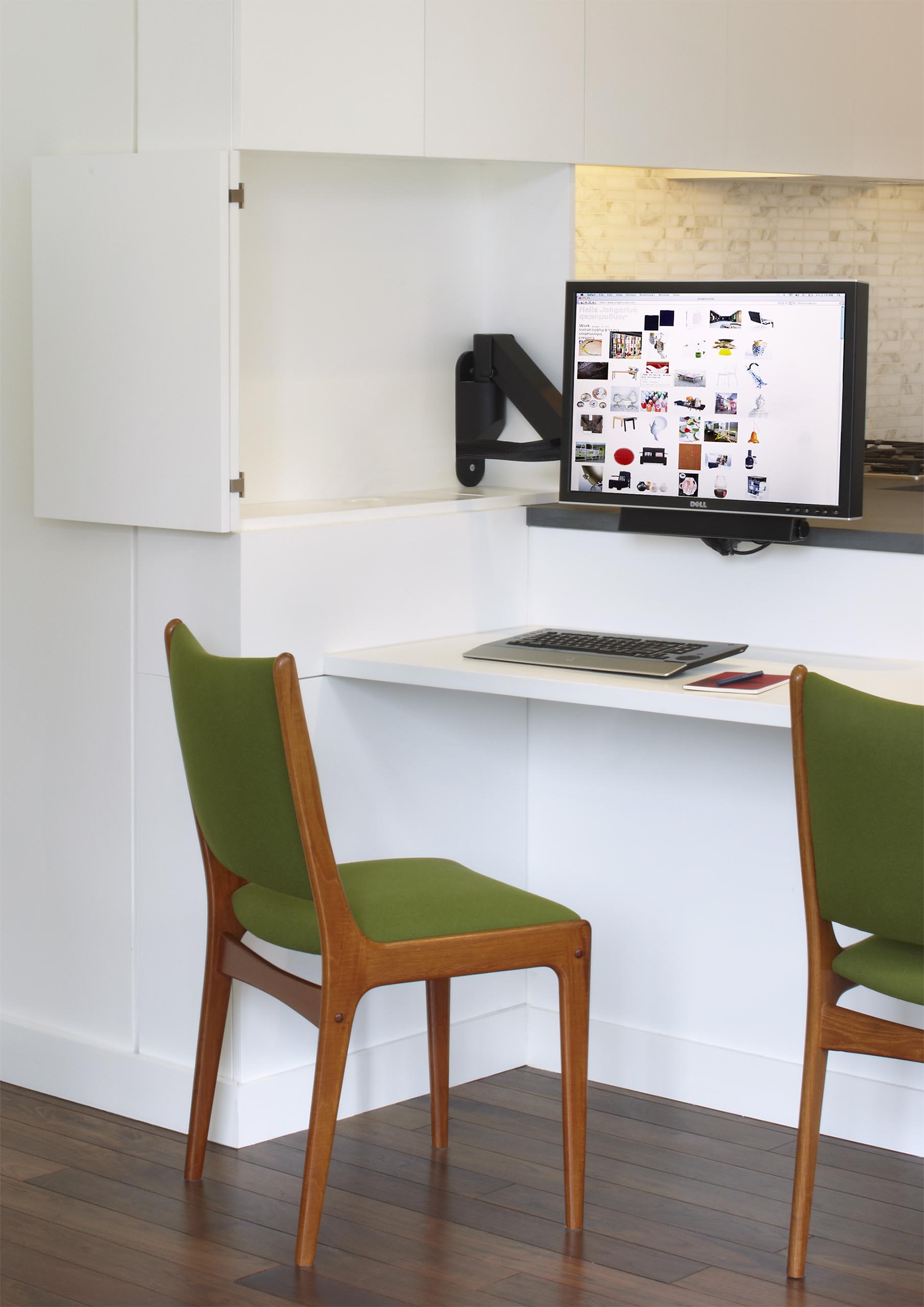 A computer monitor is hidden within the kitchen cabinets, creating a small home office.