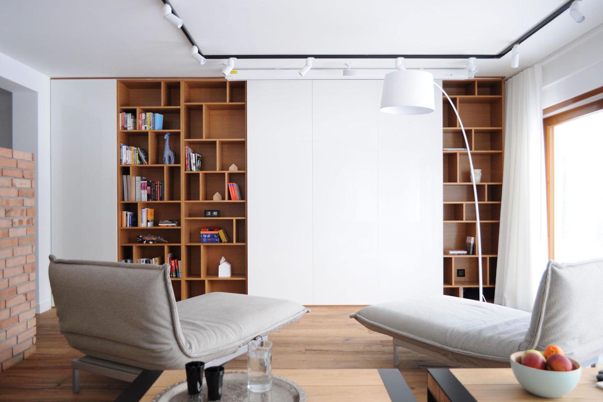 A living room with wood bookshelves has white wall panels that hide a TV.