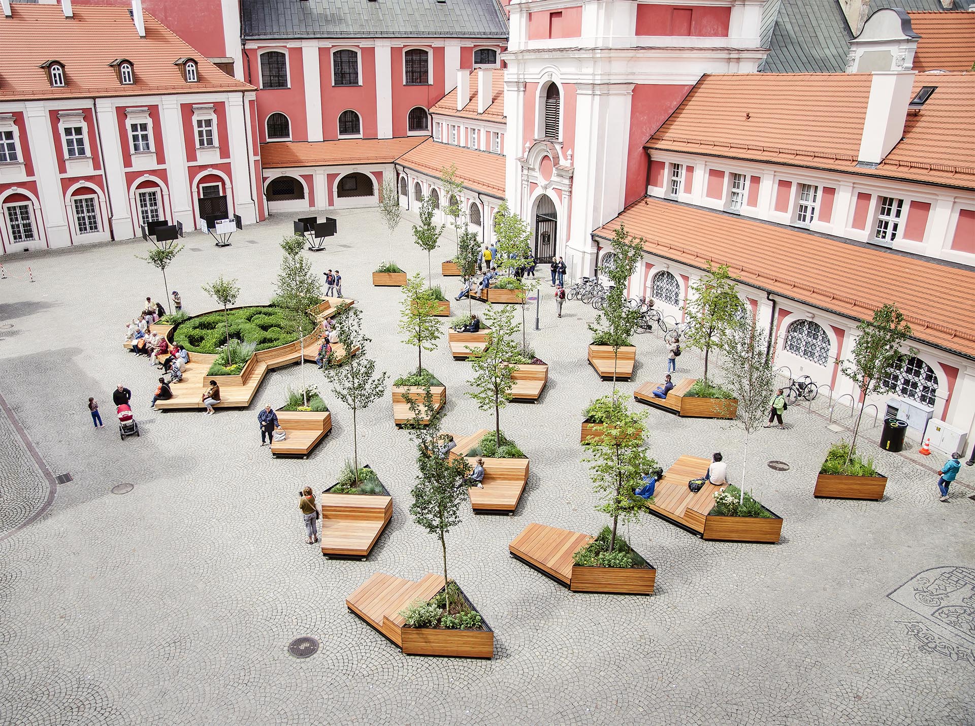 Mobile wood benches rest against triangular planters in a courtyard.