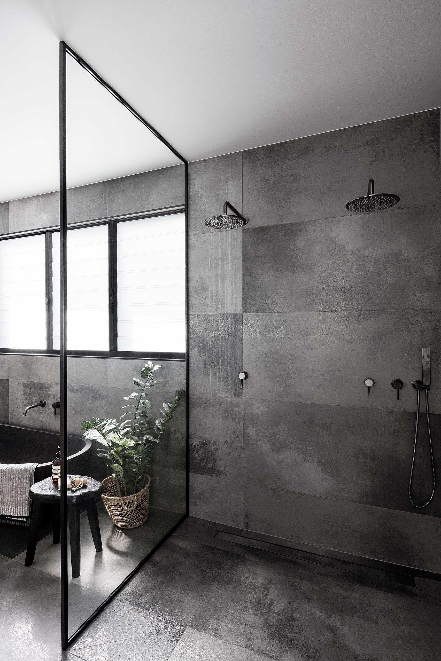 A modern bathroom with a black framed glass shower screen, large format grey tiles, and two shower heads.