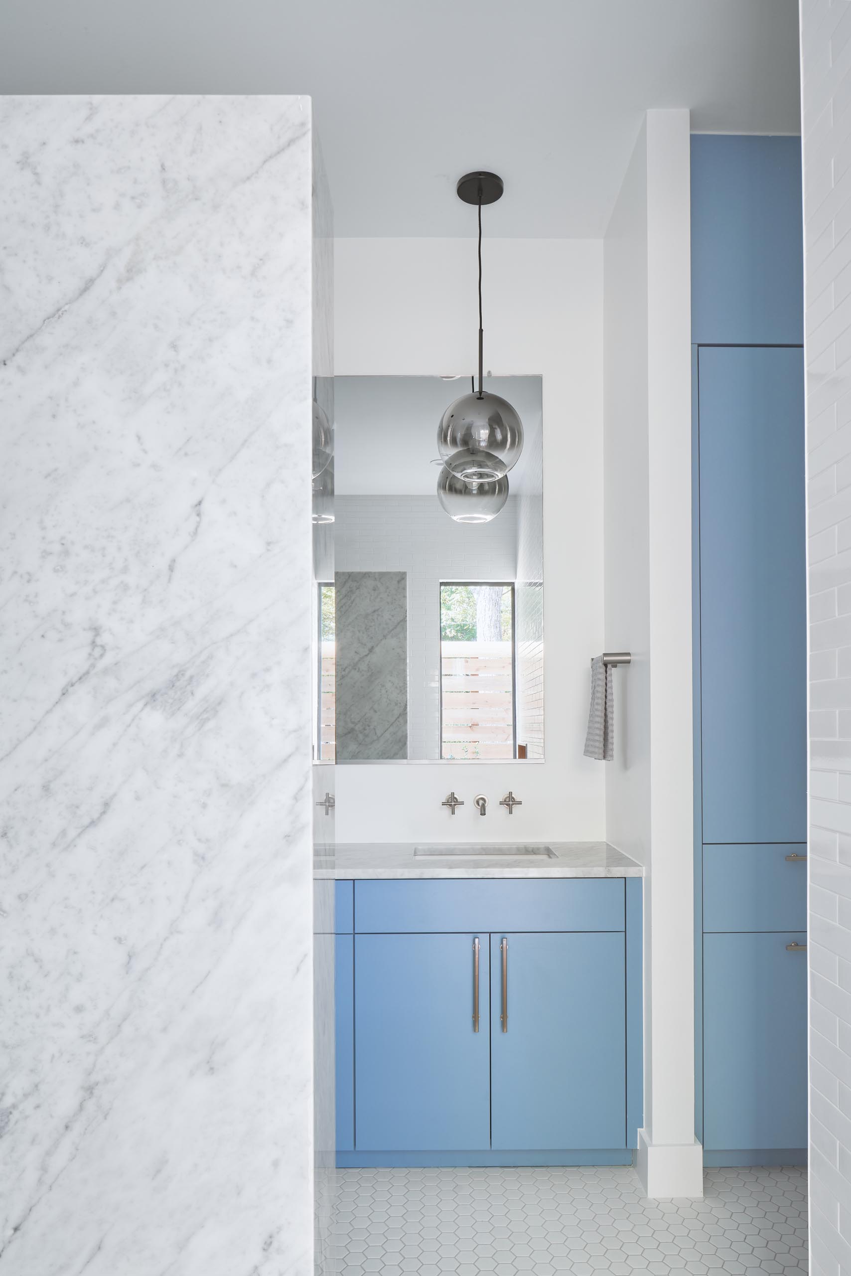 A modern bathroom with a light blue vanity and cabinets, and a marble countertop.