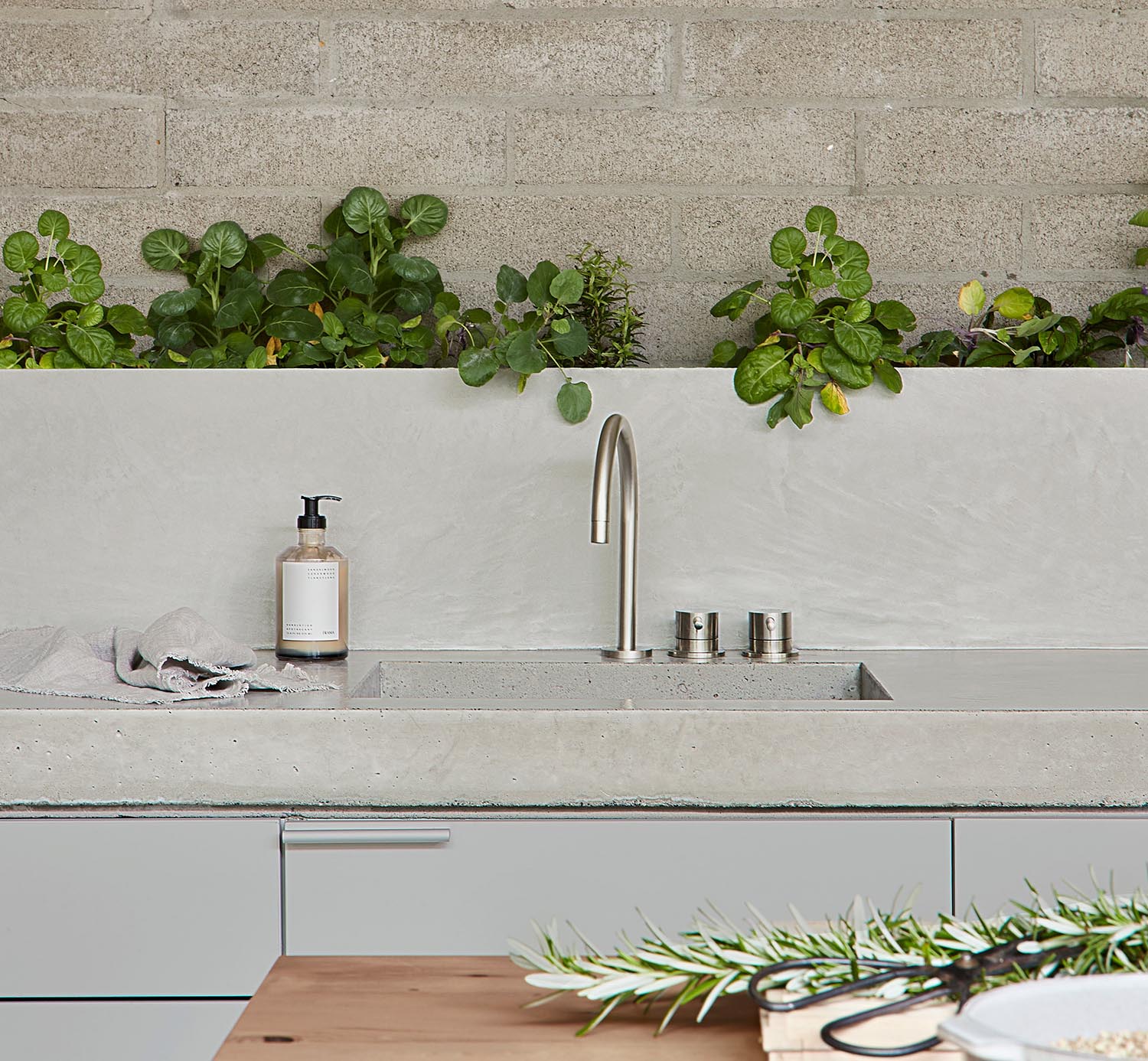 A modern concrete kitchen countertop with matching backsplash and a row of plants.