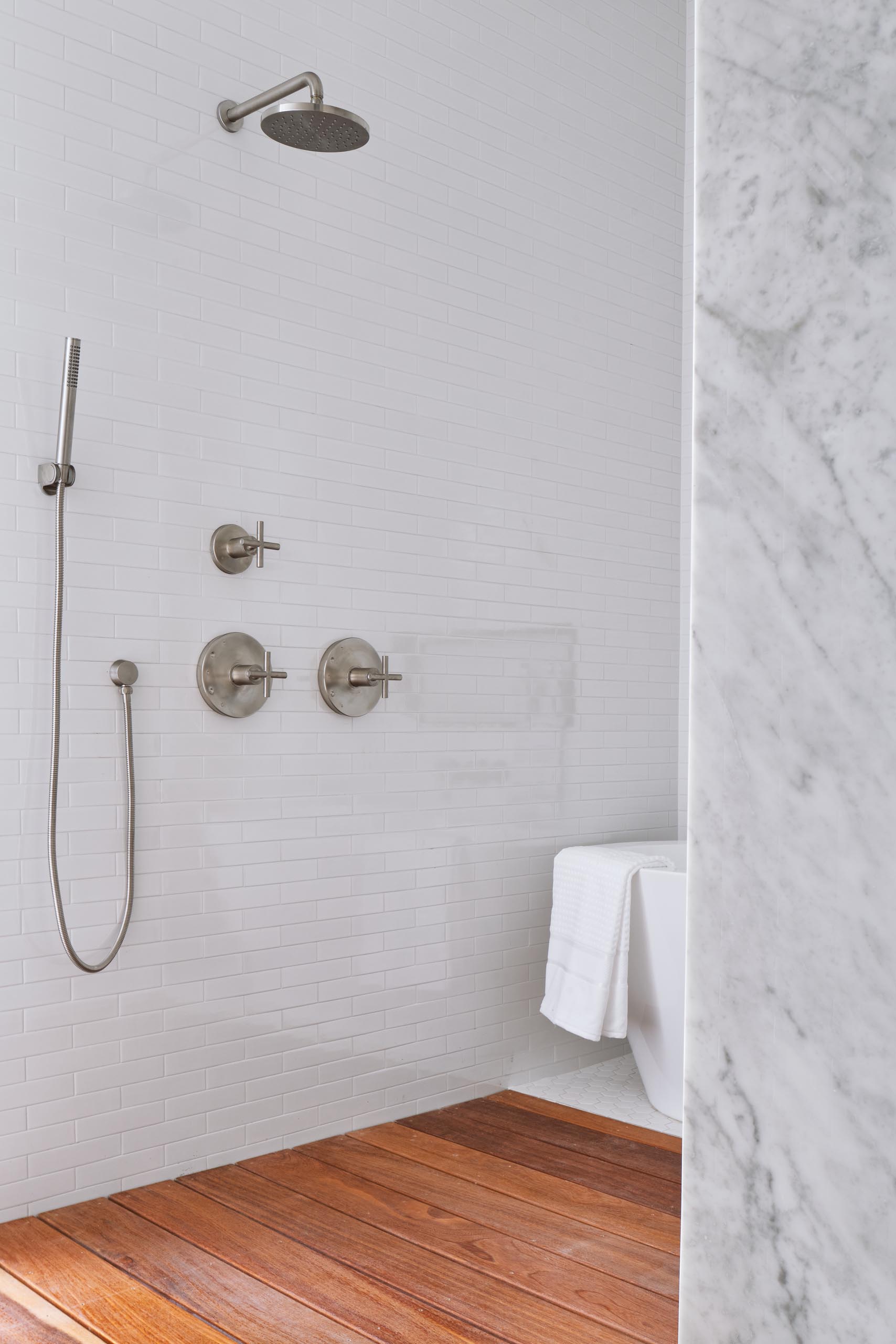 A modern white bathroom with white tiles and a wood shower floor.
