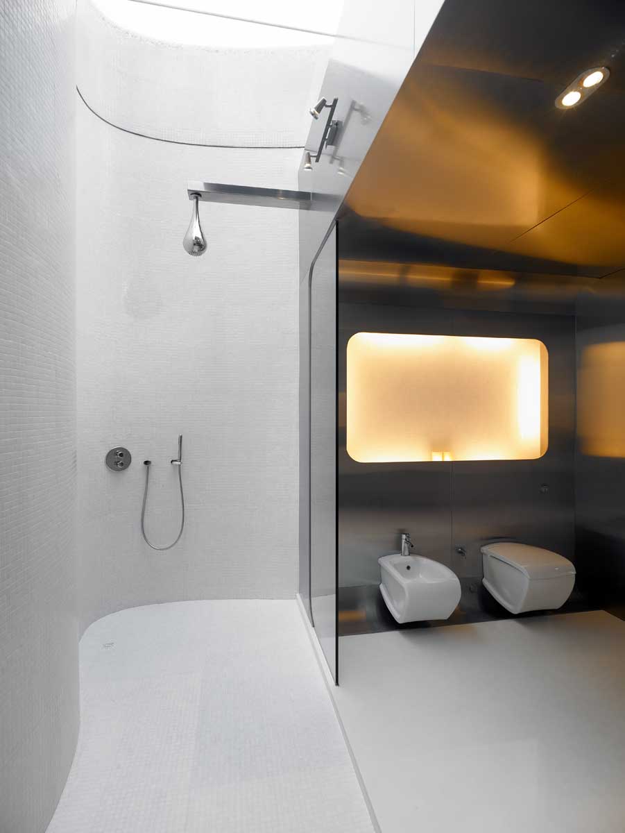 A modern bathroom with stainless steel walls, curved tiled walls, glass shower screens, and dual showers with a skylight.