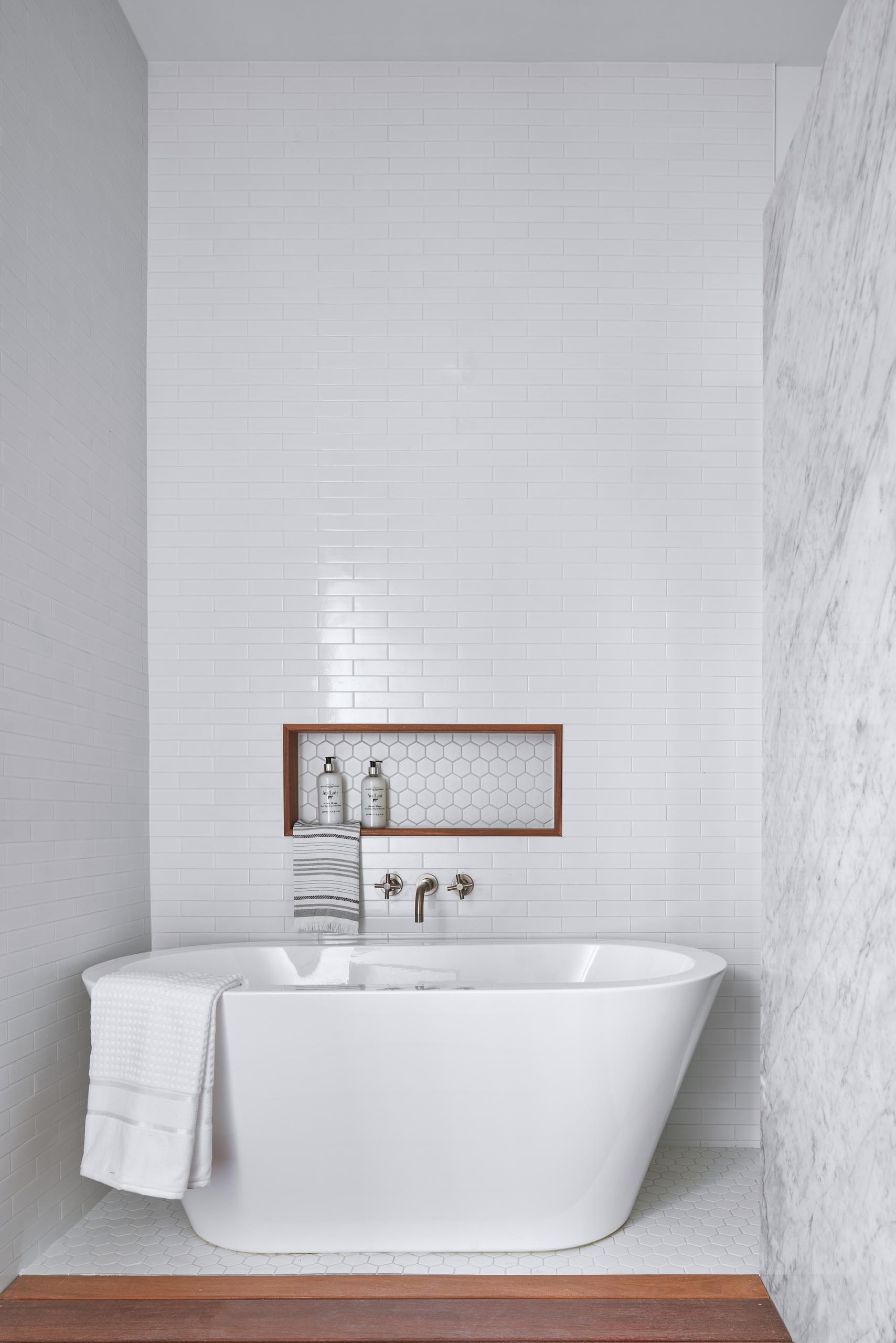 A wood lined niche above a freestanding white bathtub.