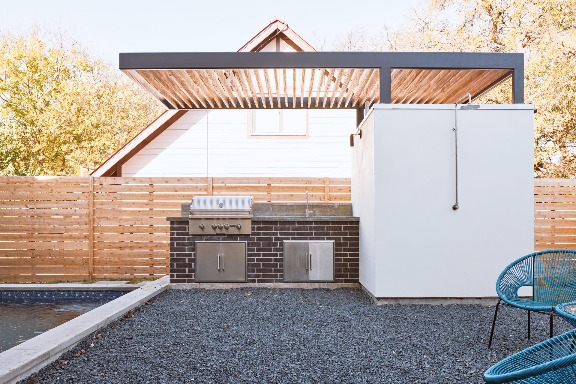 A small pool house with a bathroom has a outdoor kitchen attached.