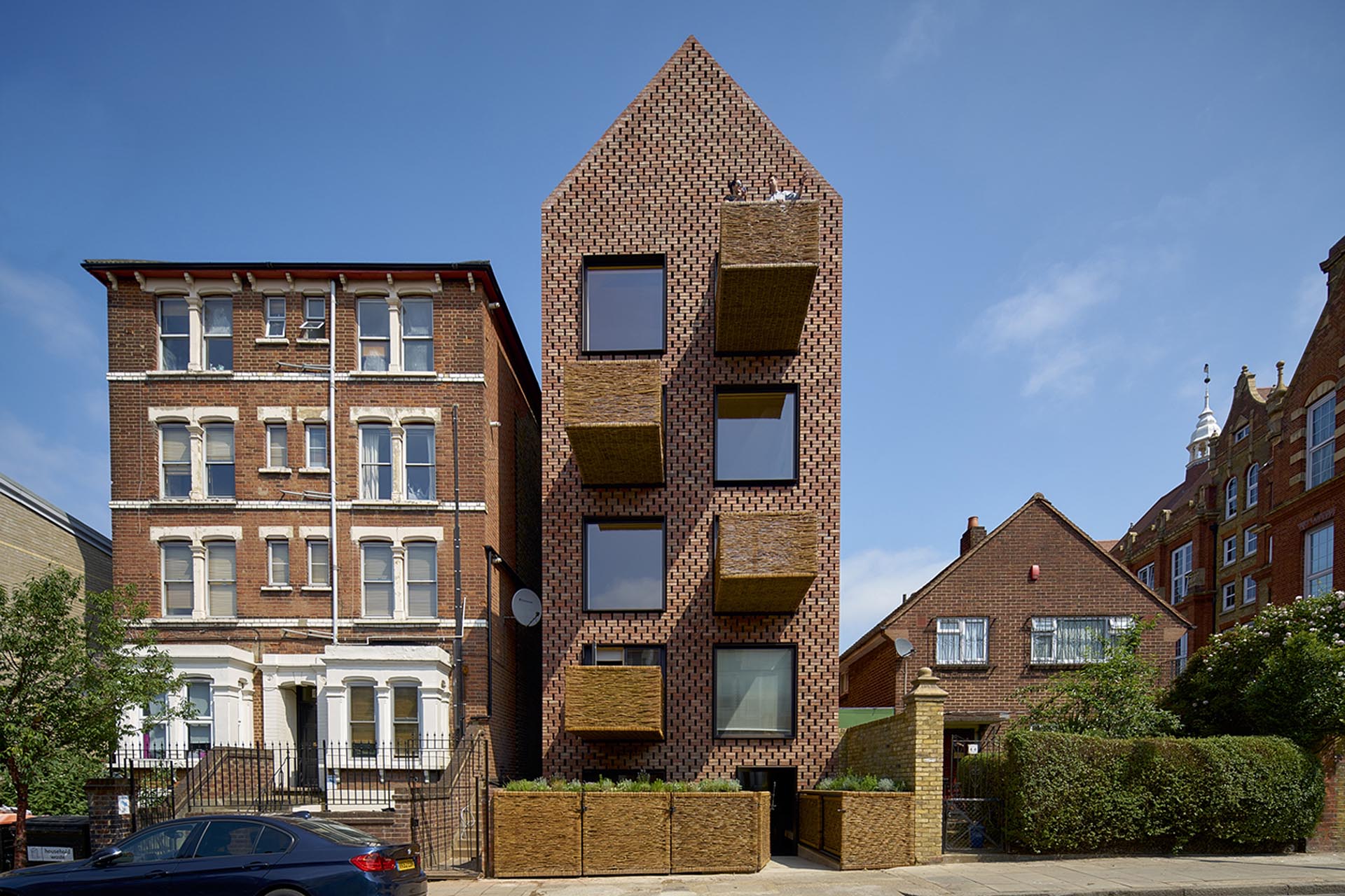 A brick building with steel window frames and protruding woven wicker balconies.