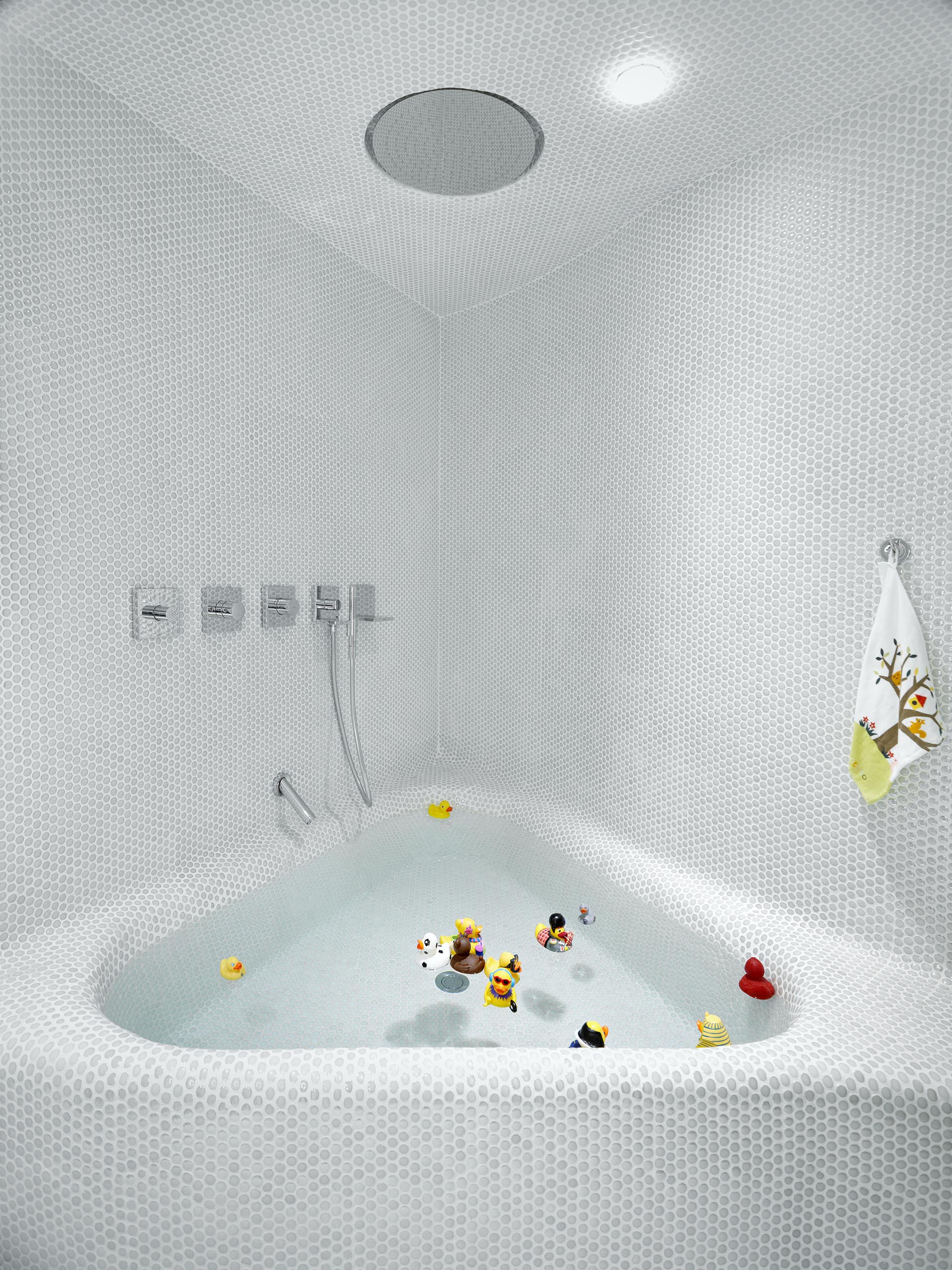 A modern white bathroom with penny tiles and a built-in triangular bath.