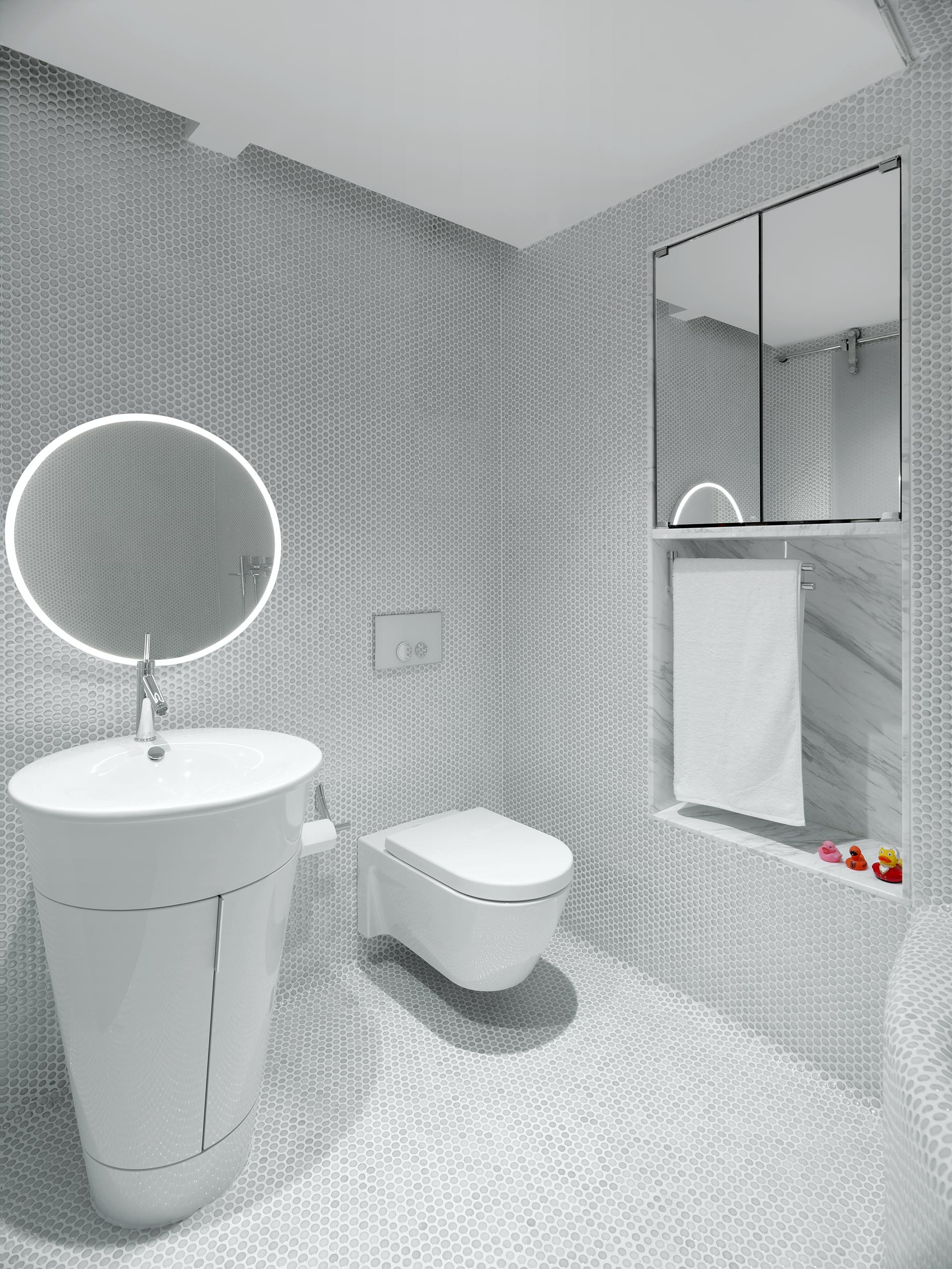 A white bathroom covered in penny tiles, that also has a built-in mirror and shelving niche.