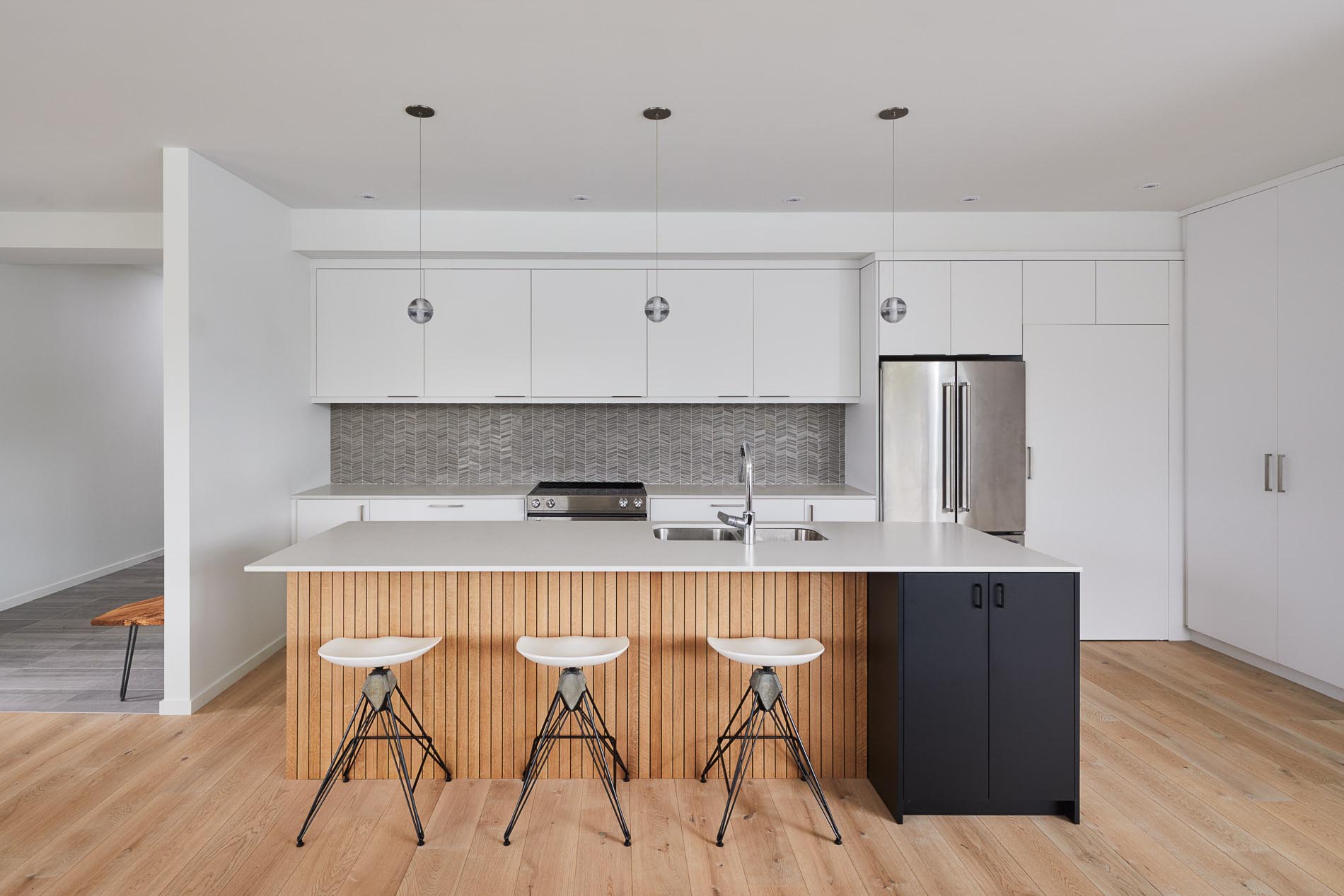 A white kitchen with a grey tile backsplash, and an island with wood and black accents.